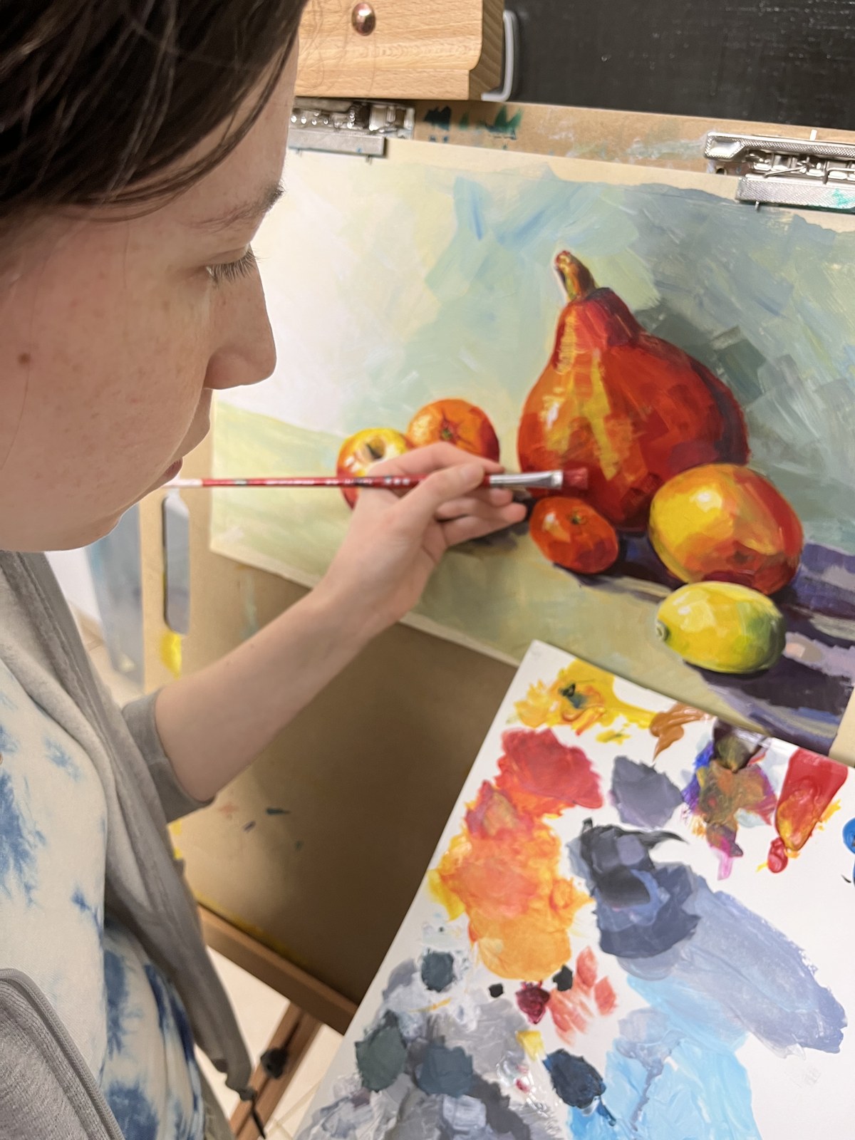 Student painting a pear and fruit still life