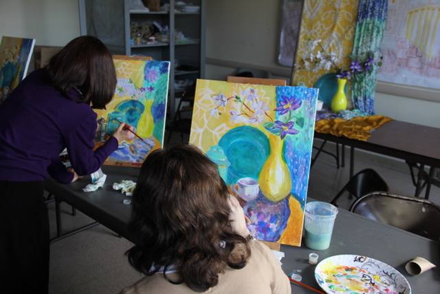 Two students painting still life with blue plate and yellow vase